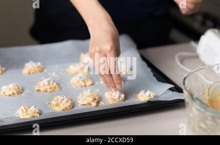 Frau, die Kokosnusskekse Teig macht und sie auf einem aranging Pfanne mit Backpapier zu Hause Nahaufnahme bedeckt Stockfoto