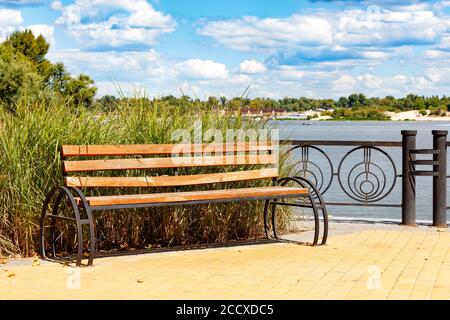 Eine Holzbank auf dem Dnipro Böschung vor dem Hintergrund von hohen Gras, einem breiten Fluss von Licht wolkigen Himmel. Stockfoto