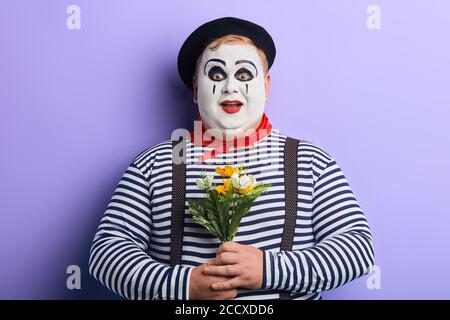 Überrascht aufgeregt Clown hält Blumen in den Händen isoliert auf weiß, gehen, um sie einem Liebhaber zu geben. Freundlichkeit, Freundschaft Stockfoto