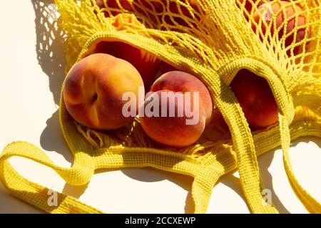 Nahaufnahme reife Pfirsiche in einem Netzbeutel oder String-Beutel auf hellgelben Hintergrund. Flach liegend. Keine Verschwendung. Stockfoto