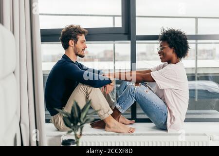 Interracial Ehepaar liebevoll zu Hause innere Umarmung, sitzen in der Nähe der grossen Fenster, Unterstützung und emotionale Ressource aus einander empfinden, ha Stockfoto