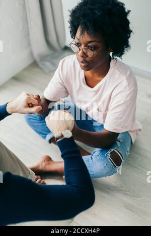 Kaukasische Freund und seiner afrikanischen Freundin Yoga praktizieren, gekreuzten Beinen sitzen, Hände halten zusammen, auf der Suche während der Sitzung auf Holz Stockfoto