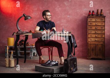 Junge kreative Schuster erfinden schicke Schuhe, volle Länge Foto Stockfoto