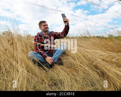 Der junge Tourist macht ein Selfie, während er im Herbstfeld sitzt. Stockfoto