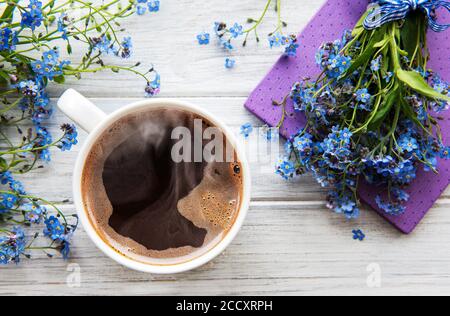 Blaue Vergissmeinnicht-Blumen, Notizbuch und eine Tasse heißen Kaffee. Das Konzept der Feiertage und Guten Morgen Wünsche. Stockfoto