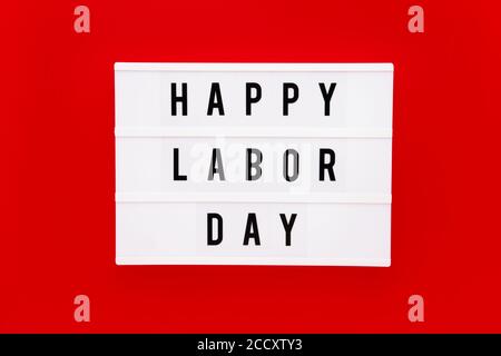 HAPPY LABOR DAY in einem Leuchtkasten auf einem leuchtend roten Hintergrund geschrieben. Labor Day-Konzept Stockfoto