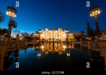 Beleuchtetes Kunstmuseum Museo de Artes y Costumbres Populares de Sevilla in einem Brunnen reflektiert, blaue Stunde, Plaza de America, Sevilla, Andalusien Stockfoto