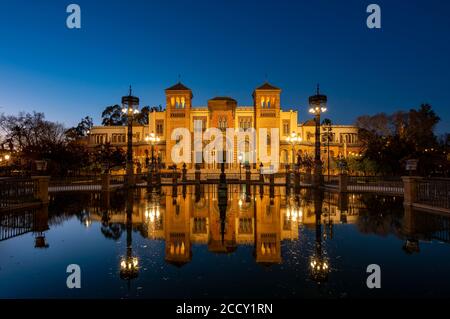 Beleuchtetes Kunstmuseum Museo de Artes y Costumbres Populares de Sevilla in einem Brunnen reflektiert, blaue Stunde, Plaza de America, Sevilla, Andalusien Stockfoto