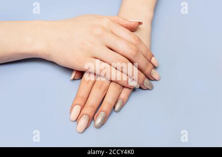 Schöne gepflegte Hände mit Maniküre und Nagellack. Blauer Pastellhintergrund. Nahaufnahme. Stockfoto