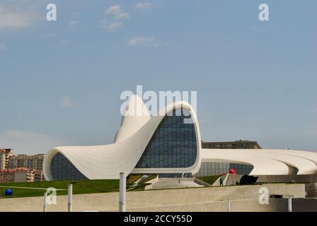 Baku Aserbaidschan. Der Eingang zum Heydar Aliyev Center, fließender, geschwungener Stil, entworfen von Zaha Hadid, mit Nachbarschaftsgebäuden als Hintergrund. Stockfoto