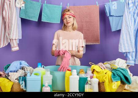 Fröhliche blonde Hausfrau in Freizeitkleidung setzen auf Schutzhandschuhe. Close up Portrait.Vorbereitung für das Waschen von Kleidung. studio erschossen. Stockfoto