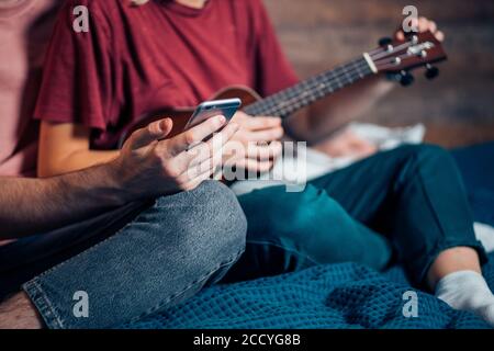 Beschnitten zwei Menschen männlich und weiblich spielen Ukulele, Studium von Video auf Smartphone Stockfoto