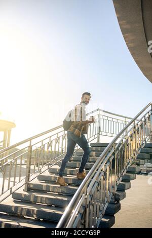 Fröhlicher Mann mit Rucksack und Kaffee Treppen steigen Stockfoto