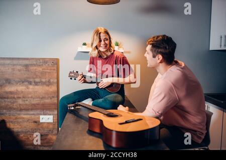 Attraktive junge kaukasische Frau in Freizeitkleidung spielen Ukulele für Mann, der ihr zuhört Stockfoto