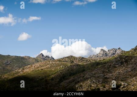 Felsige Gebirgsformationen stehen im Horizont, unter blauem Himmel und weißen Wolken. Ruhige Berglandschaft Stockfoto