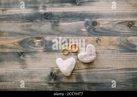 Eheringe und Brautring in Weißgold auf einer Holzstruktur mit herzförmigen Steinen. Stockfoto