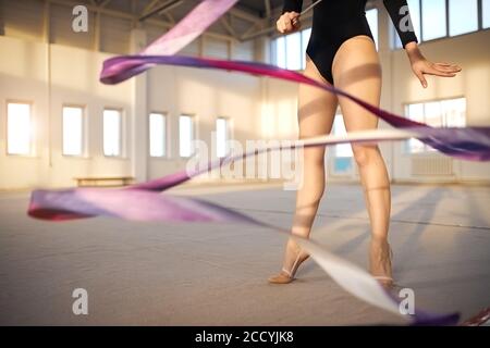 Nahansicht der langen Beine des professionellen jungen Turnertrainings mit violettem Band in der Gymnastikschule, aktives Lifestyle-Konzept Stockfoto