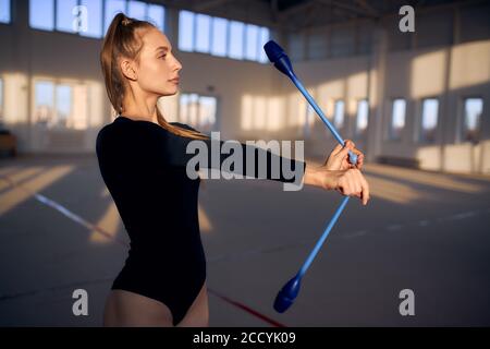 Nahaufnahme der weiblichen Turnerin, die mit blauen Schlägern im geräumigen Studio spielt, wegschaut, Seitenschuss, professionelles Sportkonzept Stockfoto