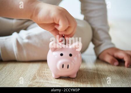 Kinderhände legen eine Münze in ein Sparschwein und Sparen Sie ihr Taschengeld Stockfoto