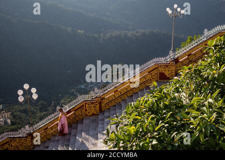 buddhistische Mönchin, die die Treppe hinuntergeht. Nonne trägt traditionelle rosa und orange Kleidung, rasierte Kopf. Kyaiktiyo Golden Rock, Mon State, Myanmar Stockfoto