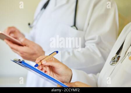 Ärztin notiert sich mit einer Kollegin auf einem Clipboard Im Hintergrund Stockfoto