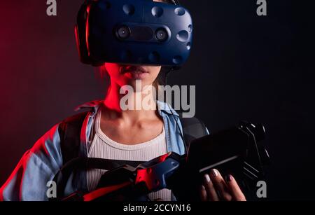 Junge kaukasische Frau hält Shooter VR, tragen Augenmaske, stehen isoliert über UV-Hintergrund Stockfoto