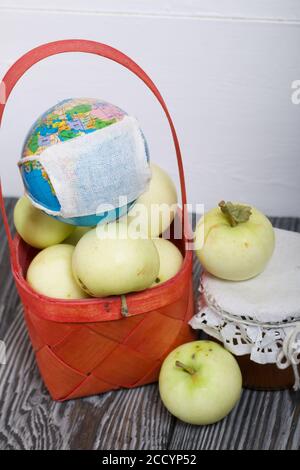 Äpfel in einem roten Korbkorb. Marmelade in Gläsern und Äpfeln in der Nähe. Obsternte. In der Nähe ist ein Globus mit einer medizinischen Maske. Stockfoto