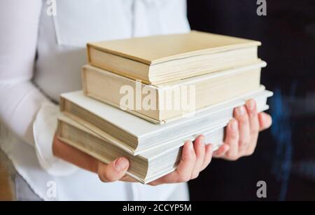 Frau trägt einen Stapel alter Bücher in einem gebrauchten Buchladen oder Bibliothek Stockfoto