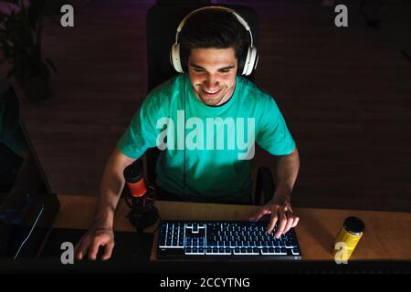 Bild von kaukasischen glücklichen Mann in Kopfhörer spielen Videospiel Am Computer, während man drinnen am Tisch sitzt Stockfoto