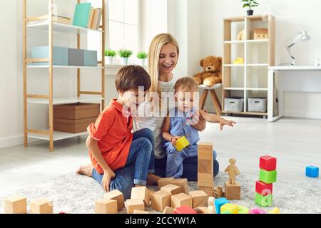 Mama und Kinder lächeln mit Spielzeug, während sie auf dem Boden im Wohnzimmer sitzen. Frohe Familie Stockfoto