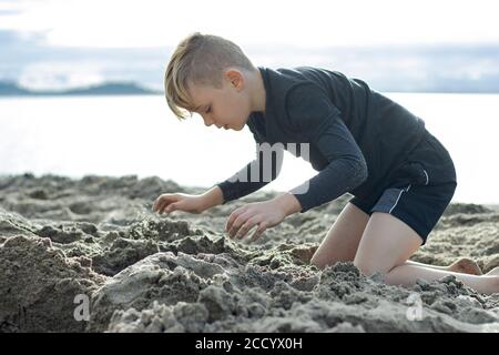 Eine Nahaufnahme eines wunderschönen Jungen, der im Sand am Strand spielt, seine Augen vor Freude verschlossen Stockfoto