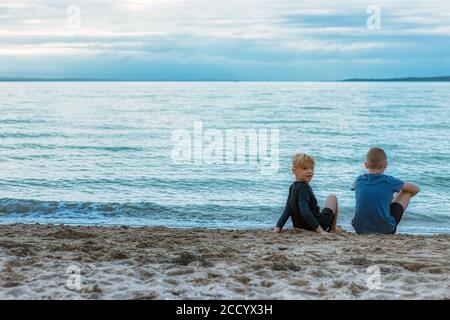 Zwei junge Brüder sitzen am Strand und schauen friedlich auf das Meer/Meer Stockfoto