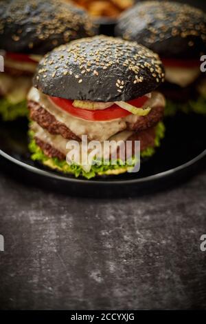 Lecker Doppel-Hamburger mit Rinderpasteten und geschmolzenem Käse mit Knusprige Zwiebel und frische Tomaten und Salat in schwarzem Brötchen Mit Sesam Stockfoto