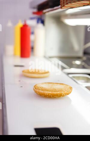 Das Hamburgerbrötchen befindet sich auf der Arbeitsfläche des Kochs. Daneben befinden sich Edelstahlbehälter mit Kochzutaten. Stockfoto
