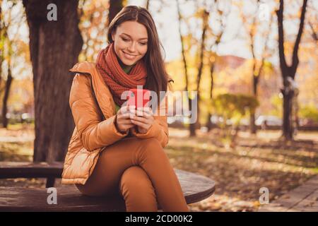 Foto von ziemlich charmante Dame lächelnd sitzen Bank halten Telefon Warte Freund eingeben senden Geo-Position in der Nähe Straße Stadtpark Tragen Schal grün Rollkragen Stockfoto