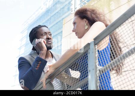 Afrikanischer Mann und europäische kaukasische Frau auf einem Spaziergang in der Stadt, Mann im Gespräch am Telefon. Sommertag. Hochwertige Fotos Stockfoto