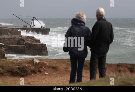 Die Leute schauen von der Klippe aus, während die Wellen am Portland Bill in Dorset gegen die Küste krachen. Stockfoto