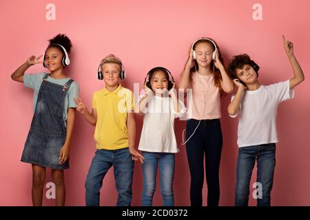 Multinationale Schüler mit Headsets, die Musik genießen oder Audio hören Bücher auf rosa Hintergrund Stockfoto