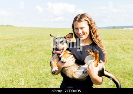 Junges Mädchen mit lockigen Haaren mit ihrem Welpen in den Armen. Mädchen hält einen Hund Stockfoto