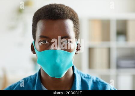 Kopf- und Schulterportrait eines jungen afroamerikanischen Mannes, der eine Maske trägt und die Kamera anschaut, während er im Postpandemic-Büro steht, Kopierraum Stockfoto