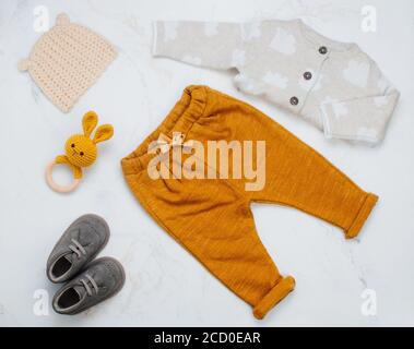 Babykleidung, Babyschühchen und Beißring auf hellem Marmorhintergrund. Draufsicht, flach liegend. Stockfoto