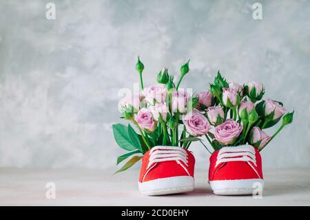 Paar rote Babyschuhe gefüllt mit Rosen Blumen. Leerzeichen für Text. Stockfoto