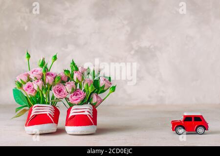 Paar rote Babyschuhe gefüllt mit Rosen Blumen und Auto Spielzeug. Leerzeichen für Text. Stockfoto