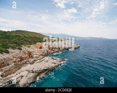 Felsige Küste in der Nähe Veslo Camping in Montenegro. Azurblaues Wasser, weiße Wellen treffen auf die Felsen, sonniger Sommertag, Luftdrohne Blick. Stockfoto