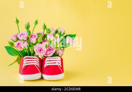 Paar rote Babyschuhe mit Rosenblüten auf gelbem Hintergrund. Leerzeichen für Text. Stockfoto