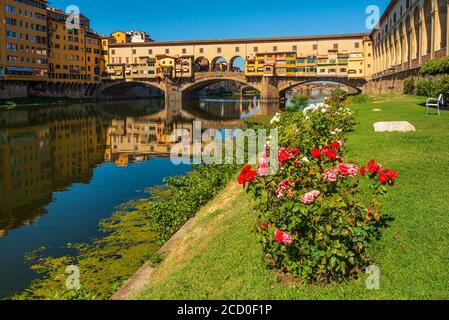 Die berühmten Florenz Ponte Vecchio Aufnahmen aus dem Arno Wasser Ebene mit Blumen im Vordergrund und Reflexionen der Brücke Stockfoto