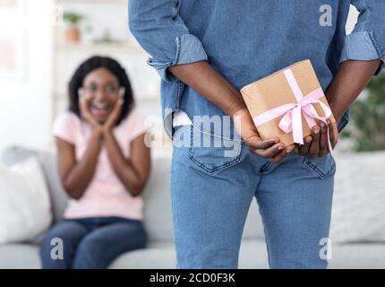 Mann hält Geschenk hinter dem Rücken für seine überraschte Freundin Stockfoto