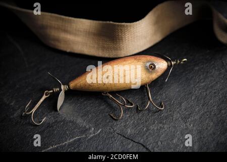 Ein Beispiel für einen alten South Bend Angelköder, oder Stecker, entwickelt, um Raubfische auf einem dunklen Schieferhintergrund neben einem alten Whicker ta angezeigt zu fangen Stockfoto