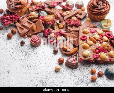 Gebrochene Tafeln Milchschokolade mit Nüssen und sublimierten Beeren, Schokoladenkuchen und Süßigkeiten auf texturiertem grauen Hintergrund, mit leerem Platz für Text Stockfoto