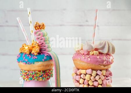 Nahaufnahme von zwei Freak-Shakes, die mit Donut, Marshmallow, Meringues, Popcorn und Marmelade auf grauem Hintergrund überziehen; selektiver Fokus Stockfoto